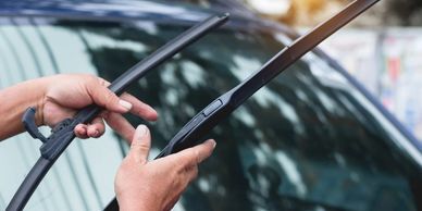 A person holding a pair of wipers in front of their car.